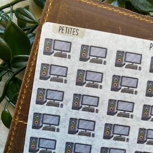 May include: A sheet of stickers featuring small computer illustrations. Each sticker shows a desktop computer with a monitor, keyboard, and tower. The word "PETITES" is printed on a label at the top. The stickers are on a brown leather surface.