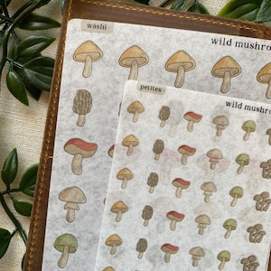May include: Close-up of mushroom-themed washi tape and sticker sheets. The washi tape features repeating mushroom illustrations, while the sticker sheets display various mushroom designs. The text "washi", "petites", and "wild mushroom" are visible.
