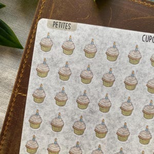 May include: Sheet of stickers featuring small cupcake illustrations with candles. The cupcakes have tan-colored bases and light brown frosting. The stickers are labeled "PETITES" in a small rectangular box.