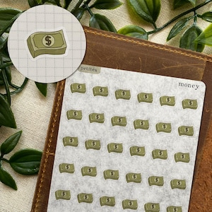 May include: A sticker sheet featuring multiple small, illustrated stacks of green paper money with a dollar sign symbol. The sheet includes the text "petites" and "money" printed in a simple black font, with a circular cutout showing a single stack.