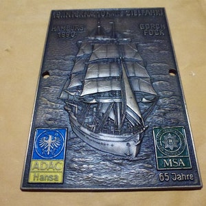 Puede incluir: Una placa de bronce que conmemora la 19ª Regata Internacional de Barcos de Vela de Formación en Hamburgo, 1990. La placa presenta un relieve del velero Gorch Fock, con los logotipos de ADAC Hansa y MSA 65 Jahre.