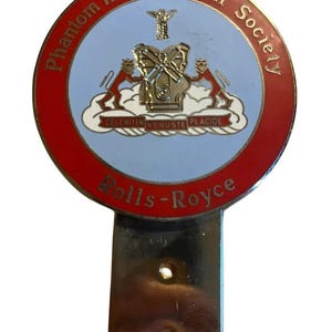 Könnte beinhalten: Ein Vintage Rolls-Royce Phantom III Technical Society Emblem. Das runde Emblem hat einen roten Rand mit dem Text "Phantom III Technical Society" und "Rolls-Royce". Die Mitte hat einen hellblauen Hintergrund mit einem detaillierten Wappen.