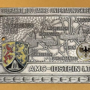 May include: A silver-coloured metal plaque commemorating "ZIELFAHRT 100 JAHRE UNTERTAUNUSKREIS" from 1967. The plaque features a map with town names, a coat of arms, and the text "AMC-IDSTEIN i.Ts."