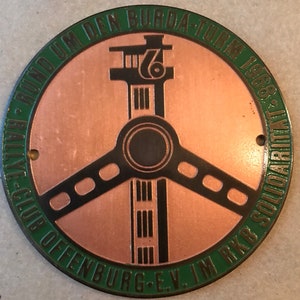 May include: A green and copper round badge with the text "Rallye-Club Offenburg e.V. im KKB Solidaritat Rund um den Burda-Turm 1968" and a stylized image of a tower with a steering wheel.
