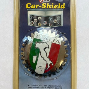 Peut inclure: Un emblème de calandre de voiture dans un emballage en plastique transparent. L'emblème présente les couleurs du drapeau italien et un contour de la carte de l'Italie. L'emballage indique "Car-Shield" et comprend le texte "3 DIMENSIONAL DEEP ETCHED FINISH".