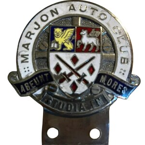 Könnte beinhalten: Vintage Marjon Auto Club Emblem. Das runde Emblem mit weißem Rand zeigt den Clubnamen. In der Mitte befindet sich ein Schilddesign mit einem Löwen, einem Pferd, gekreuzten Schwertern und den lateinischen Phrasen "ABEUNT STUDIA IN MORES".
