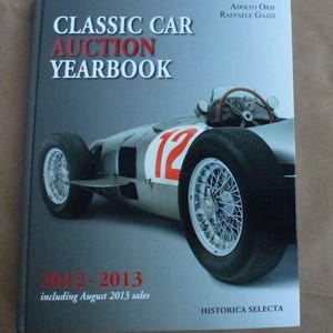 May include: A book titled "CLASSIC CAR AUCTION YEARBOOK" with a silver race car on the cover. The car has the number 12 in red. The book's title and the years 2012-2013 are in red. The authors are Adolfo Orsi and Raffaele Gazzi.