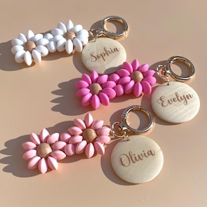May include: Three pink and white flower-shaped keychains with wooden tags engraved with the names Sophia, Evelyn, and Olivia.