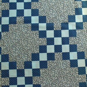 May include: A patchwork quilt with a repeating pattern of blue and light blue squares. The squares are arranged in a checkerboard design, with a floral pattern in the background.