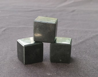 May include: Three black cube-shaped objects stacked on top of each other on a black fabric surface.