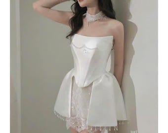 May include: A white strapless dress with a lace skirt and a satin bodice. The dress has a fitted bodice and a flowing skirt. The dress is decorated with pearls.