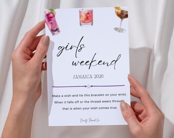 May include: A white card with the words "girls weekend JAMAICA 2026" in black script, held by hands. The card features watercolor illustrations of cocktails and a purple string bracelet. Text on the card reads, "Make a wish and tie this bracelet on your wrist."