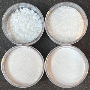 May include: Four clear plastic containers with lids, each filled with a different type of white glitter. The glitter ranges in size from fine to coarse.