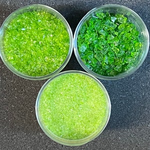 May include: Three glass jars filled with different sizes of green glass pieces. The glass pieces are clear and have a slight sparkle.