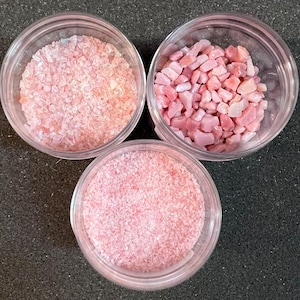 May include: Three small glass jars filled with pink and white crystals. The crystals are different sizes and shapes.