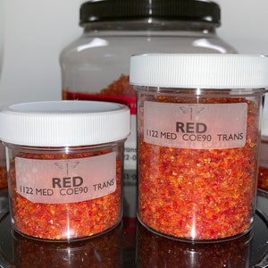 May include: Two clear glass jars with white lids filled with red and orange glass frit. The labels on the jars read "RED 1122 MED COE90 TRANS".