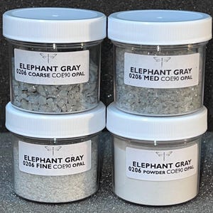 May include: Four small glass jars with white lids containing different sizes of gray opal. The labels on the jars read "Elephant Gray 0206 Coarse COE90 Opal", "Elephant Gray 0206 Med COE90 Opal", "Elephant Gray 0206 Fine COE90 Opal", and "Elephant Gray 0206 Powder COE90 Opal".