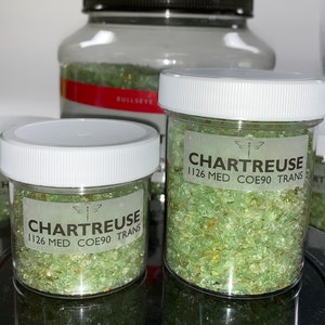 May include: Two clear glass jars filled with green and gold glass pieces. The jars have white lids and labels that read "Chartreuse 1126 Med COE90 Trans".