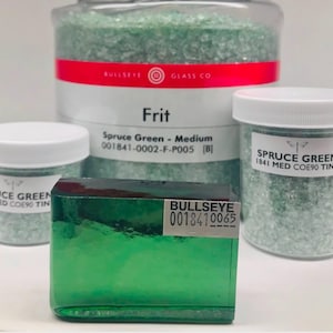 May include: An assortment of glass frit and a green glass block. The frit is in clear jars with white lids and a larger container with a red band. The labels read "Spruce Green" and "Frit". The glass block has a label with the text "Bullseye".