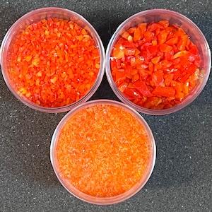 May include: Three clear glass containers filled with orange glass glitter. The glitter is in different sizes and shapes.
