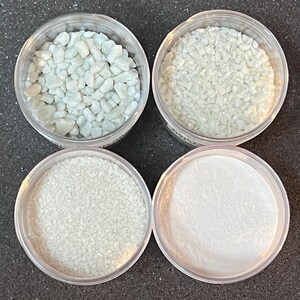 May include: Four clear plastic containers filled with different sizes of white iridescent glitter. The glitter is in various shapes, including small, medium, and large pieces.