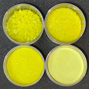 May include: Four clear plastic containers with lids, each containing a different type of yellow powder or crystals. The powders range in texture from fine to coarse.