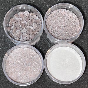 May include: Four clear plastic containers filled with different sizes of white and pink iridescent glitter. The glitter is in various sizes, from fine powder to small chunks.