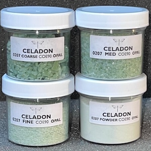 May include: Four glass jars with white lids containing different sizes of green glass beads labeled "Celadon" with the size and COE number. The jars are labeled "Coarse", "Med", "Fine", and "Powder".