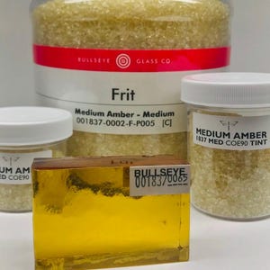 May include: A close-up of a glass frit jar labeled "Medium Amber - Medium 001837-0002-F-P005 [C]" with a smaller jar of the same frit labeled "MEDIUM AMBER 1837 MED COE90 TINT". A sample of the frit is shown in a clear glass block.