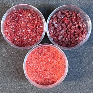 May include: Three small glass jars filled with red, orange, and burgundy colored glass glitter. The glitter is in various sizes and shapes.