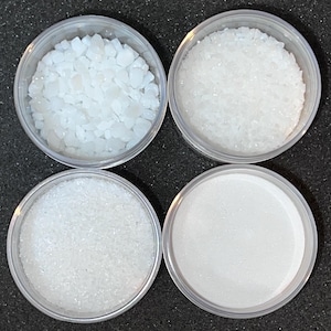 May include: Four clear plastic containers filled with different sizes of white crystals. The crystals are arranged in a grid pattern.