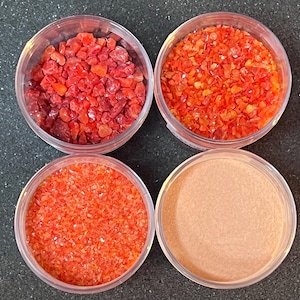 May include: Four small glass jars filled with different sizes of red and orange glass glitter. The glitter is in various shapes and sizes.