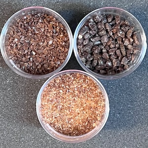 May include: Three clear glass containers filled with different types of brown, granulated chocolate. The chocolate is in various shapes and sizes.