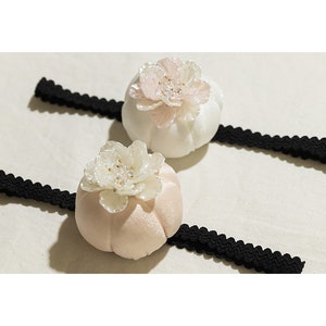 May include: Two white and pink fabric hair clips with black elastic bands. Each clip features a pearl-like flower with a rhinestone center.