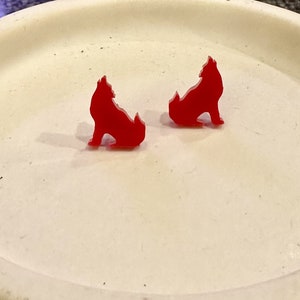 May include: A pair of red wolf silhouette earrings. The earrings are made of acrylic and are about 1 inch in size.
