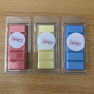 Könnte beinhalten: Drei Wachsschmelzen in durchsichtiger Plastikverpackung. Die Wachsschmelzen sind in drei verschiedenen Farben: rosa, gelb und blau. Jede Wachsschmelze hat ein weißes rundes Etikett mit dem Text "Wax Bombs Handmade with Love".