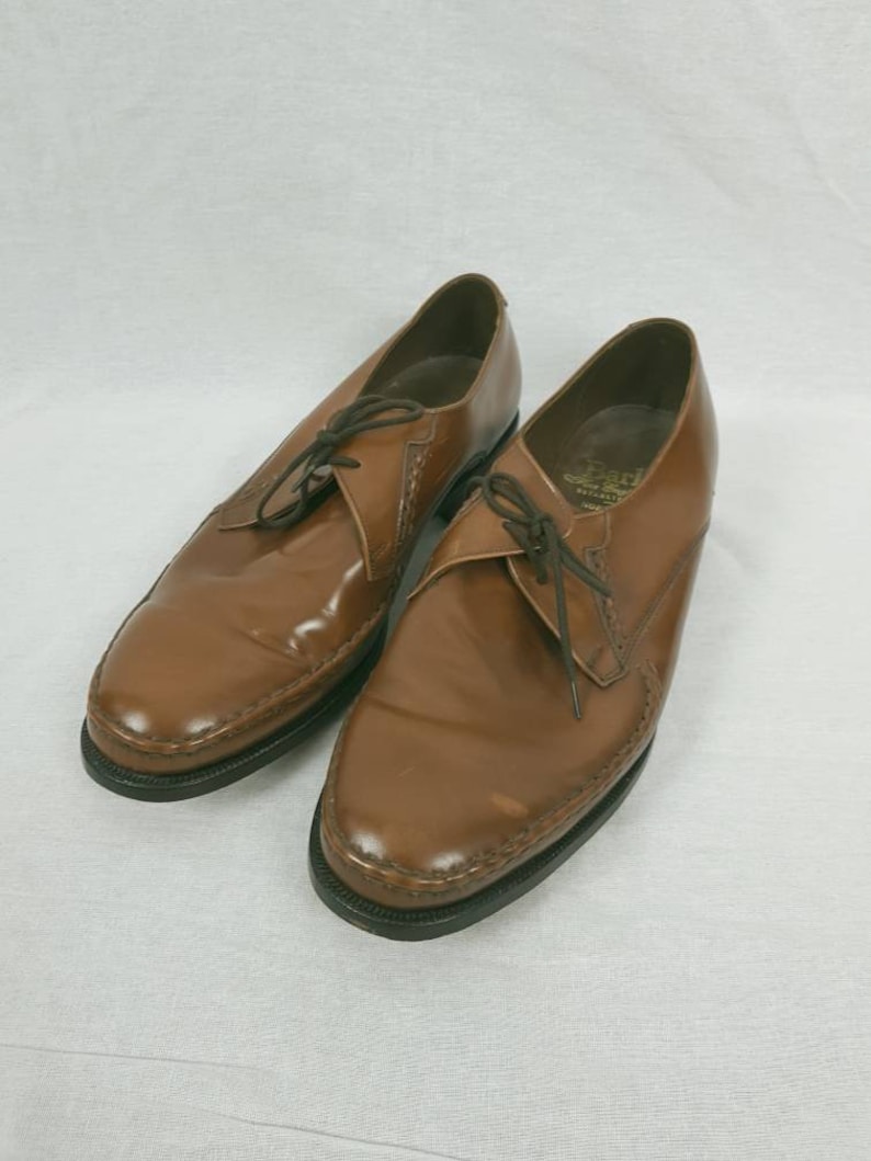 May include: A pair of brown leather lace-up shoes with a pointed toe and a stitched detail around the edge.