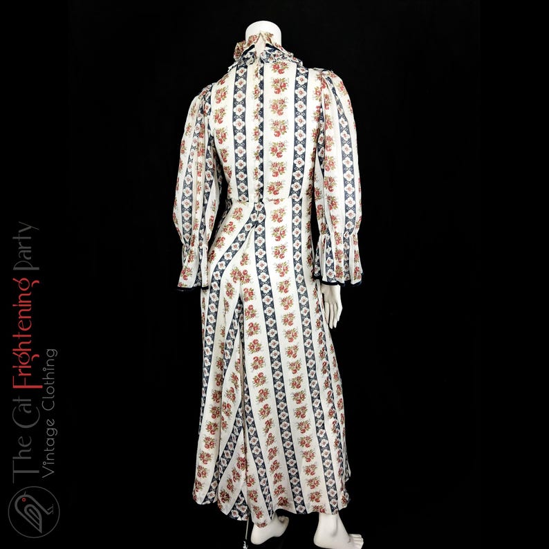 May include: A white maxi dress with a floral print and blue and white stripes. The dress has a high neck and long sleeves with ruffles at the cuffs.