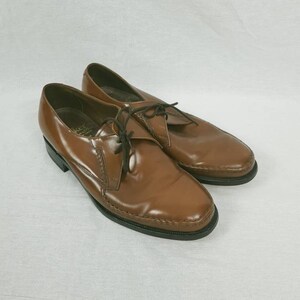 May include: A pair of brown leather lace-up shoes with a pointed toe. The shoes have a black rubber sole and a stitched design around the toe.