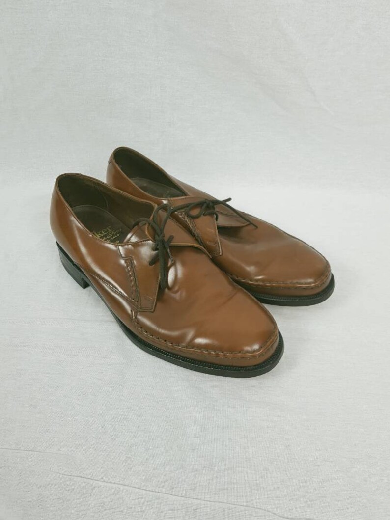 May include: A pair of brown leather lace-up shoes with a pointed toe. The shoes have a black rubber sole and a stitched design around the toe.