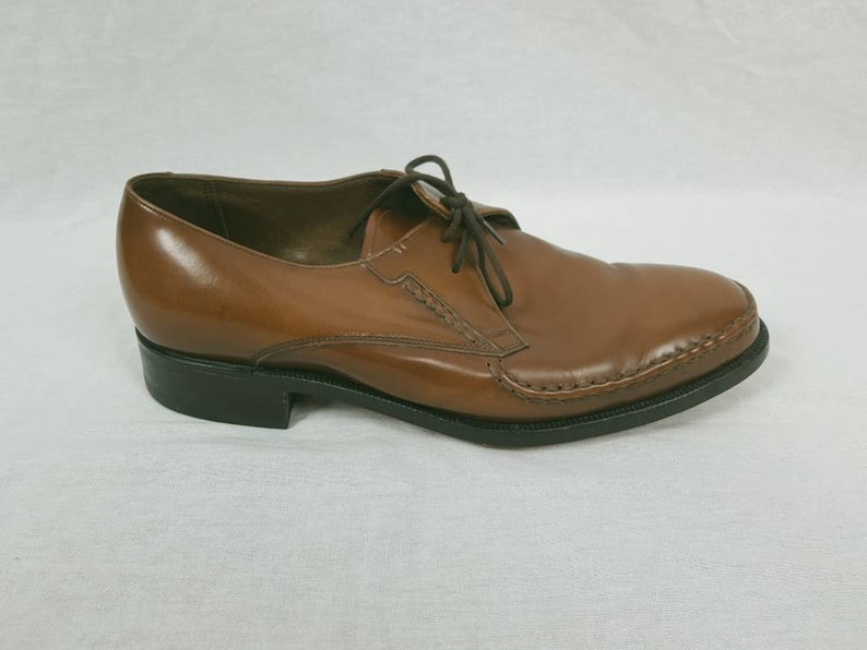May include: Brown leather lace-up dress shoes with a stitched detail around the toe and a black rubber sole.