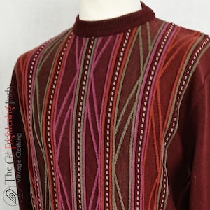May include: A burgundy-colored sweater with a mock neck and a patterned design. The pattern features vertical stripes in shades of red, pink, and orange, accented with white dotted lines. The sweater is displayed on a mannequin.