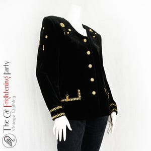May include: A black velvet blazer with gold buttons and trim. The blazer has a collar and a single-breasted closure.