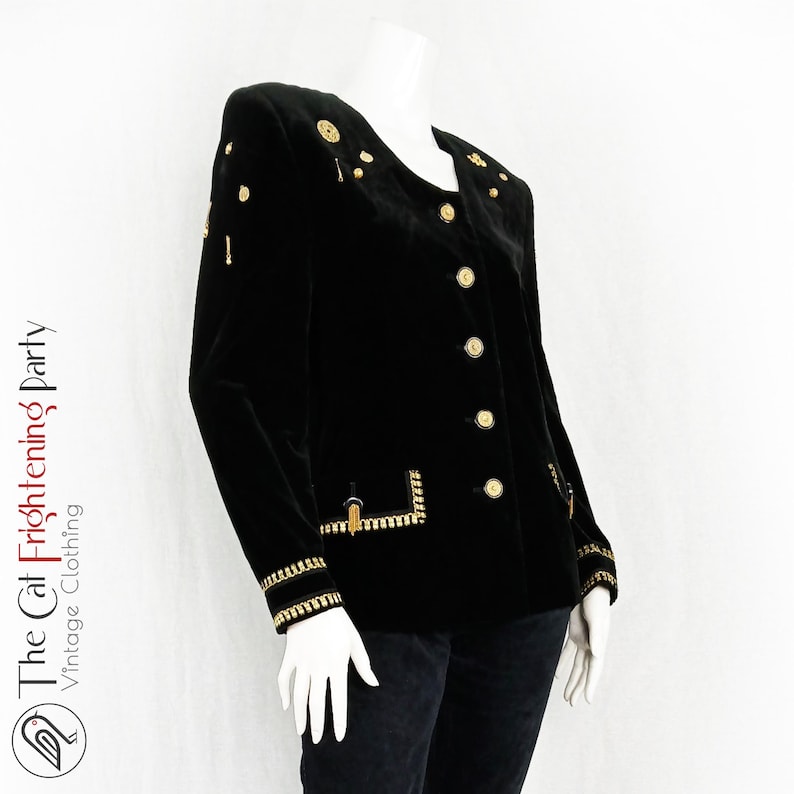 May include: A black velvet blazer with gold buttons and trim. The blazer has a collar and a single-breasted closure.