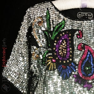 Pu&ograve; includere: Top nero vintage ricoperto di paillettes argentate, con un colorato design floreale e paisley di paillettes. Il top ha uno scollo tondo e maniche corte. L'etichetta recita "Jean for Joseph Le Bon, Paris, W. Germany."