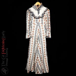 May include: A white maxi dress with a floral print and a ruffled collar. The dress has long sleeves and a fitted bodice.