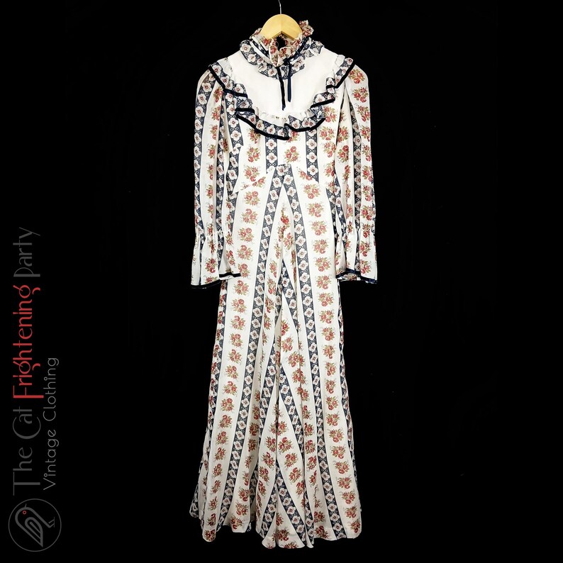 May include: A white maxi dress with a floral print and a ruffled collar. The dress has long sleeves and a fitted bodice.