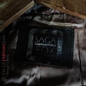 Op de afbeelding: Close-up van een zwart leren label met witte tekst die "SAGA FOX" luidt.