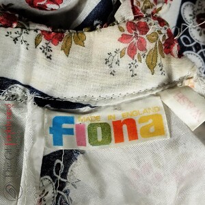 May include: A white fabric with a floral print and a blue and white striped pattern. The fabric has a label that says "Fiona Made in England".