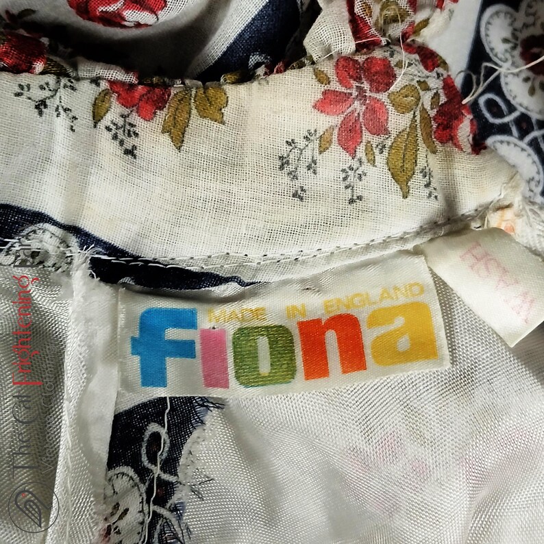 May include: A white fabric with a floral print and a blue and white striped pattern. The fabric has a label that says "Fiona Made in England".